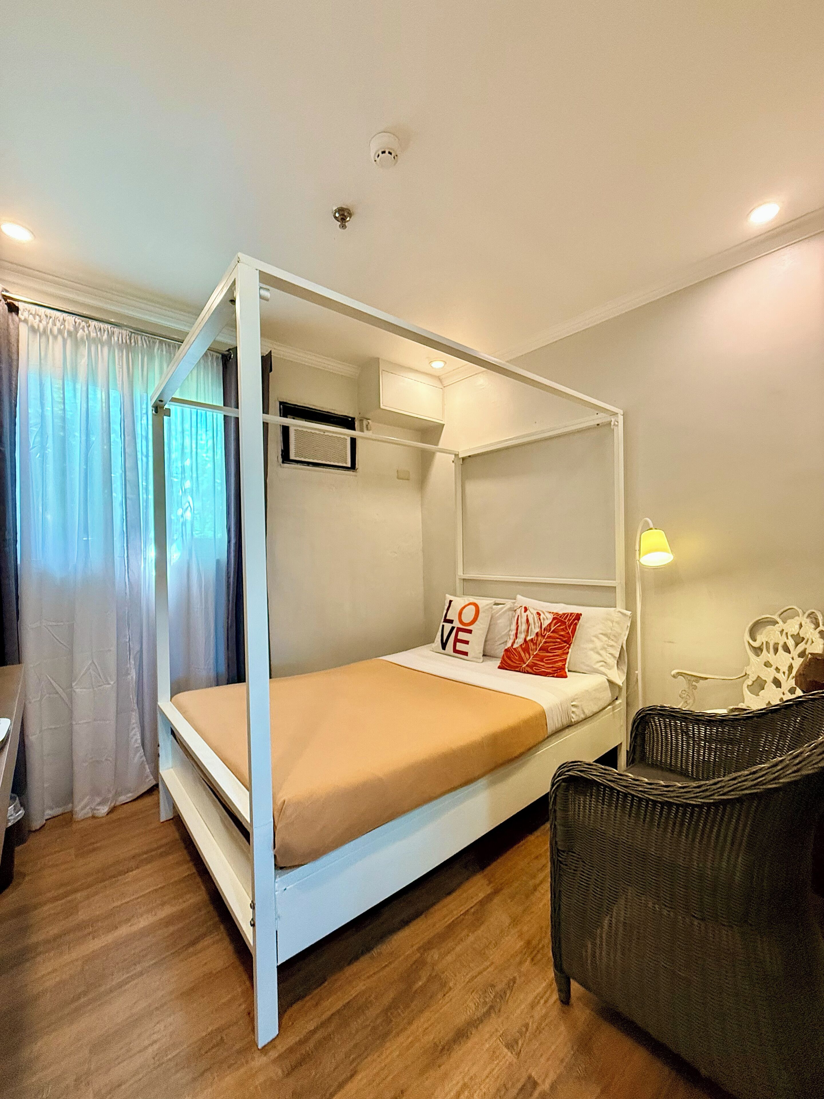 Una habitación con una cama con dosel, una silla, una lámpara y un ventanal con cortinas.