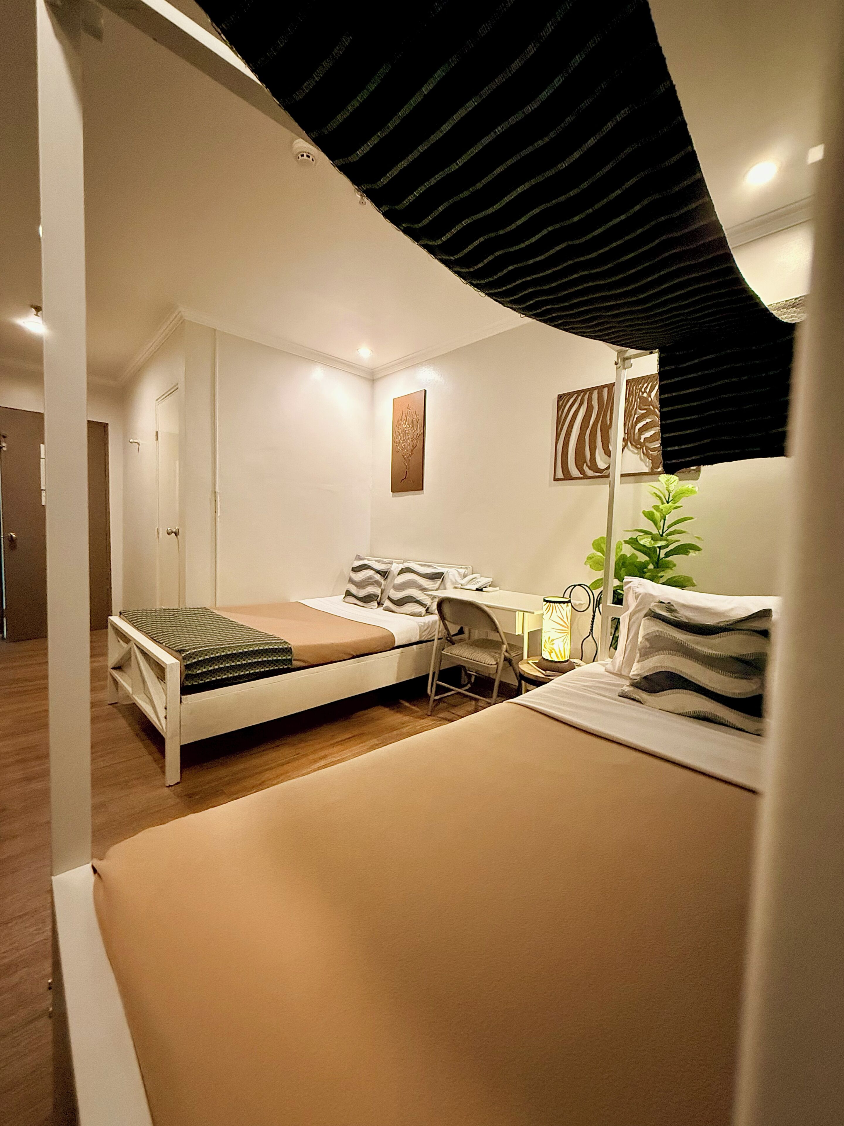 Un dormitorio con cama, escritorio, silla, lámpara y planta.