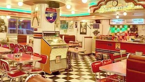 Um restaurante com chão xadrez, cabines vermelhas e um jukebox.