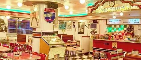 Un restaurante con suelo a cuadros, puestos tapizados de rojo y un juke box.