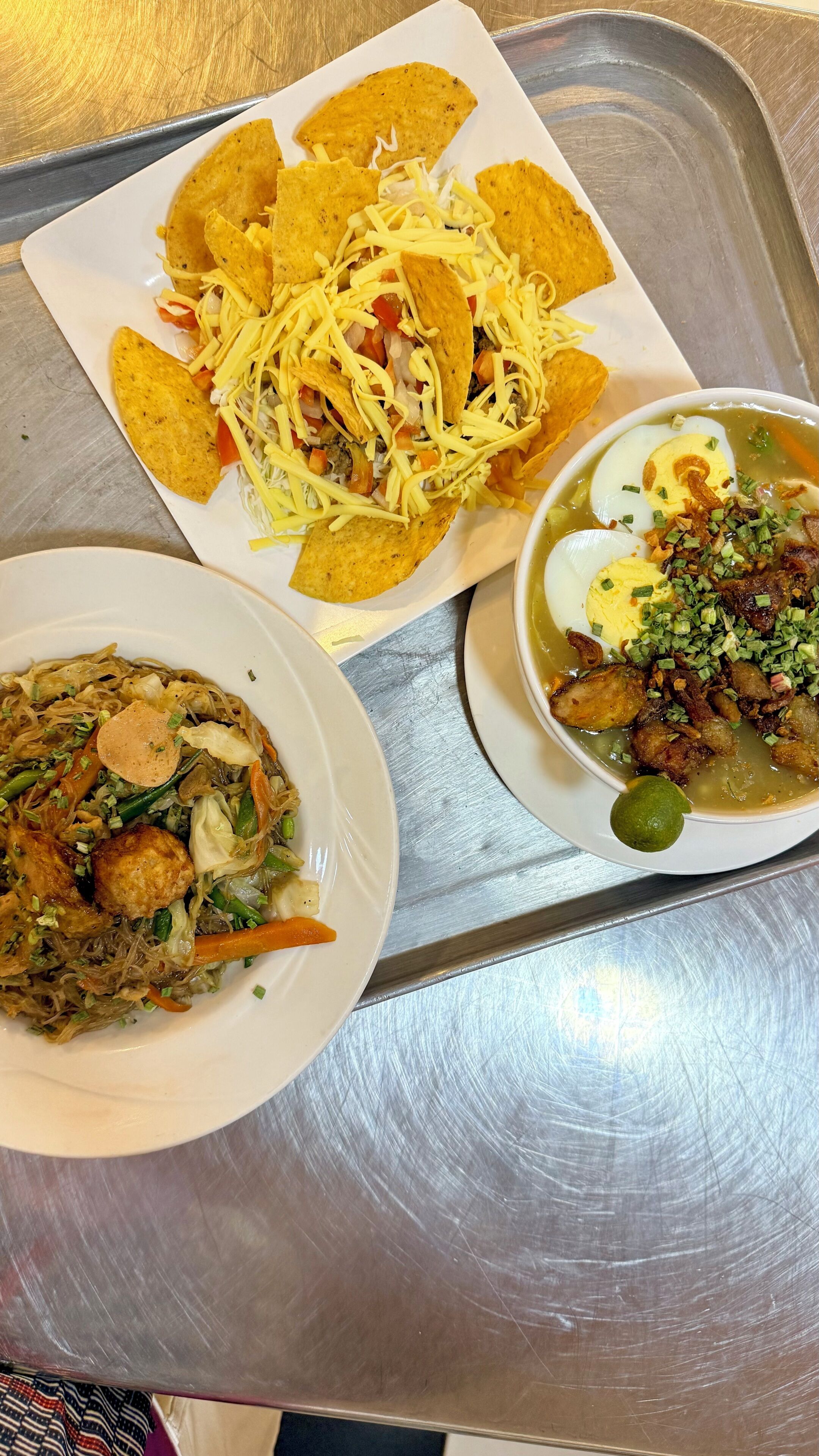 A tray with three dishes: a plate of nachos, a bowl of soup, and a plate of noodles.