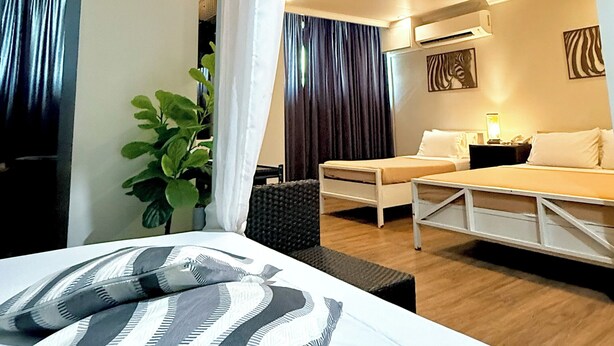 Quarto de hotel com cama, escrivaninha, cadeira, planta e luminária de teto.