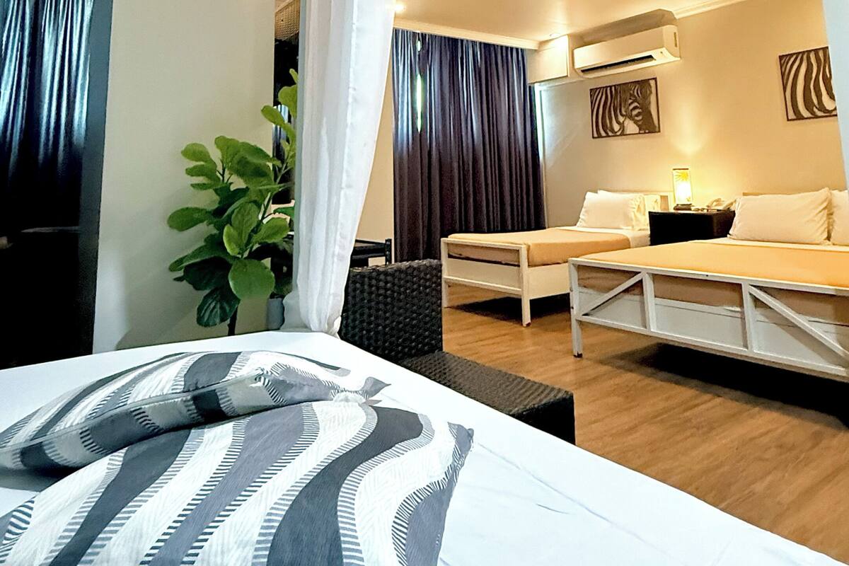 A hotel room with a bed, a desk, a chair, a plant, and a ceiling light fixture.