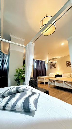 A hotel room with a bed, a desk, a chair, a plant, and a ceiling light fixture. - Hotel Tiffany - Laoag (Laoag)
