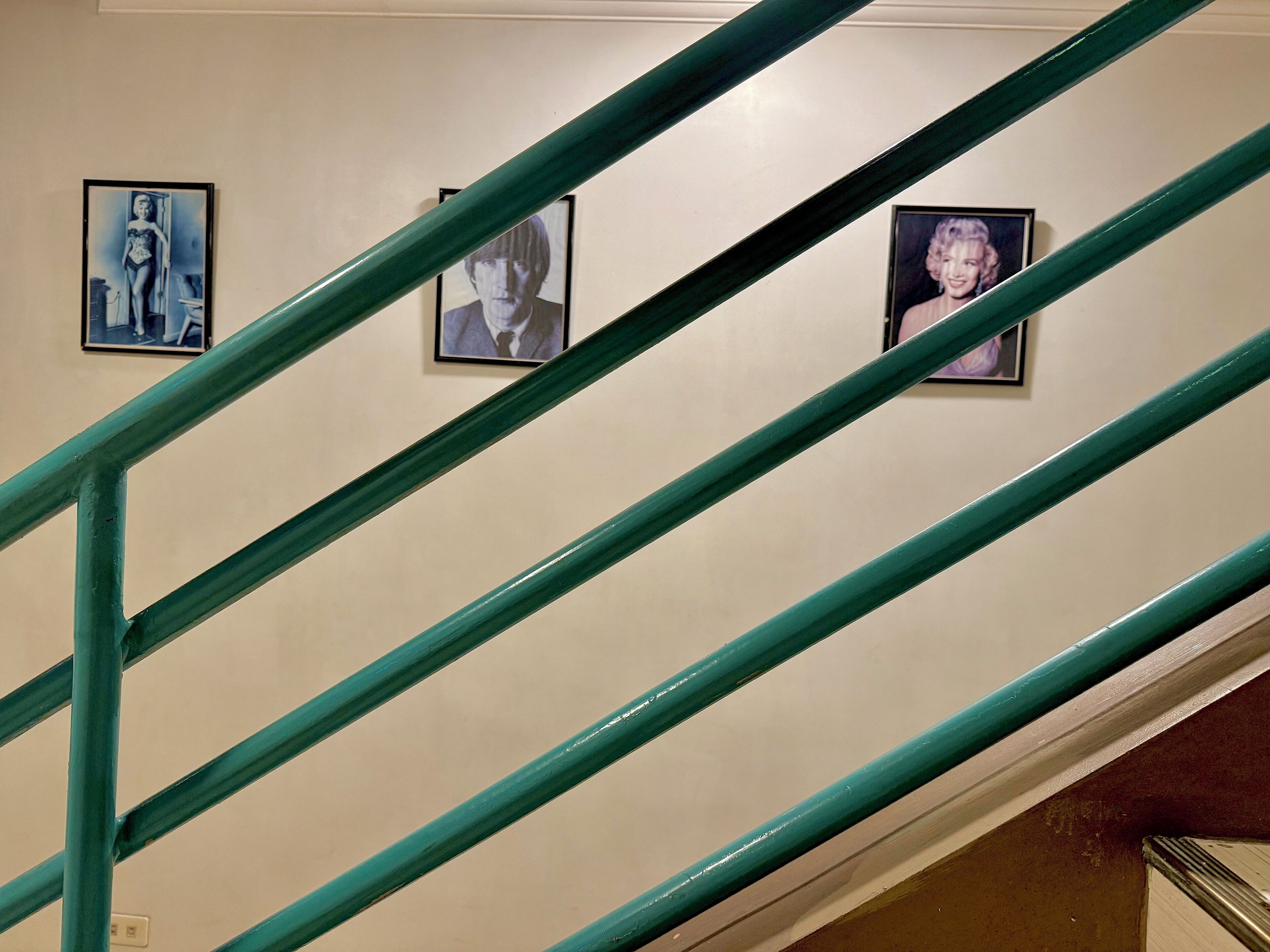 A staircase with green railings and three framed pictures on the wall.