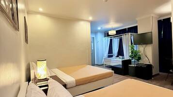 Une chambre d’hôtel avec deux lits, une télévision, une plante et un ventilateur de plafond.