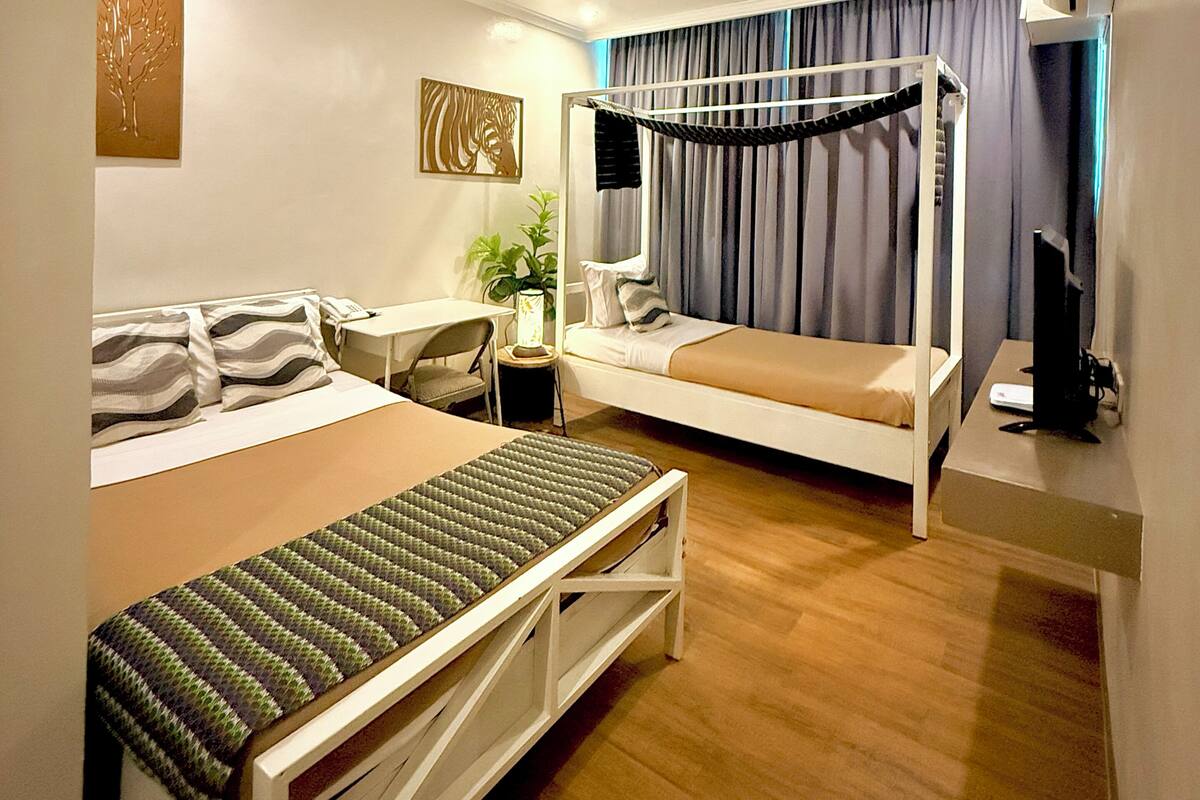 A modern hotel room with a bunk bed, a desk with a chair, a bedside table with a lamp, and a television.