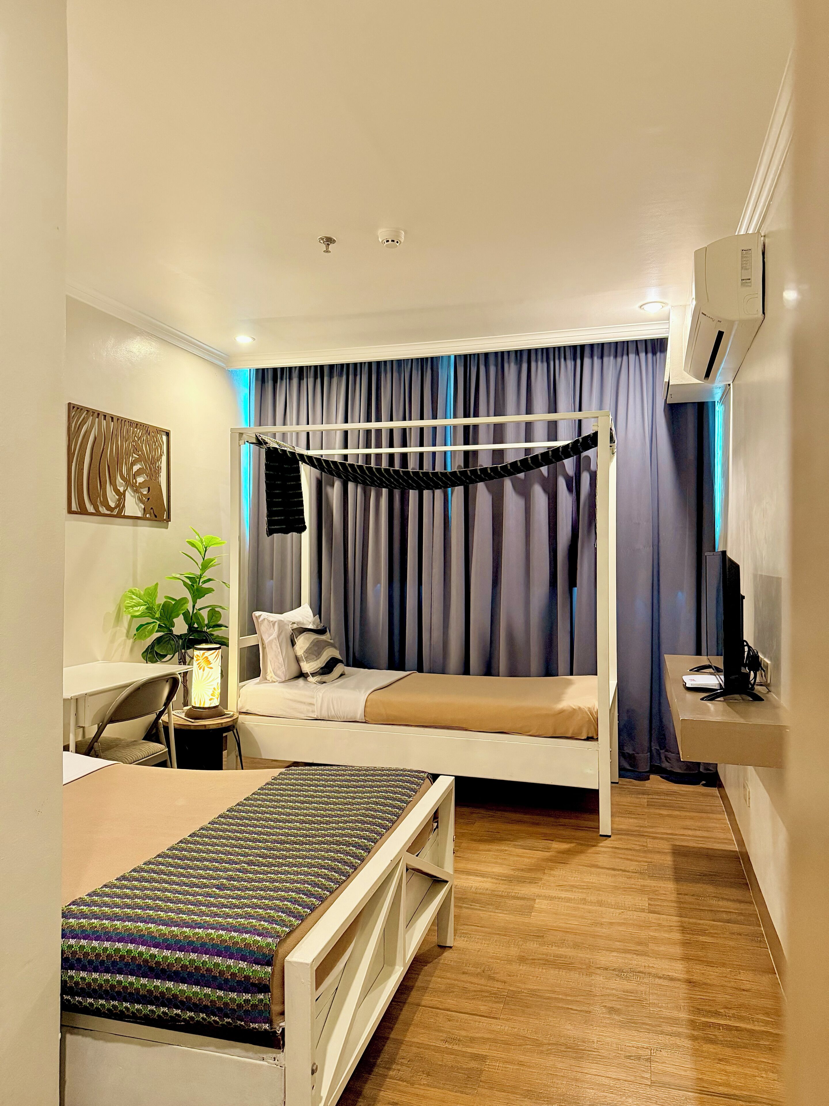 Een slaapkamer met een bed, nachtkastje, stoel, bureau, lamp en een plant.