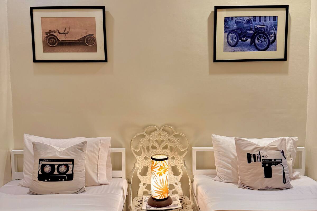 A room with two beds, a nightstand with a lamp, and two framed pictures on the wall.