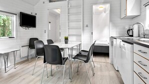 Een moderne keuken met witte kasten, een eethoek met zwarte stoelen en een aan de muur bevestigde televisie.