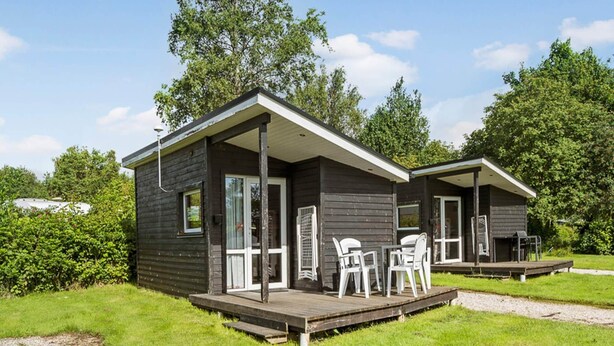 Een chalet met twee verdiepingen, een terras en een zitgedeelte buiten.