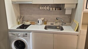 A compact kitchen with a washing machine, a sink, and a countertop with various kitchen items. - Beautiful Sunset view in Seongsan Ilchulbong (Jeju-si)