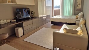 A modern hotel room with a bed, a sofa, a TV, and a balcony with curtains. - Beautiful Sunset view in Seongsan Ilchulbong (Jeju-si)