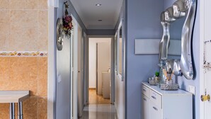 A hallway with a tiled floor, a kitchen area with cabinets and a sink, and a decorative mirror on the wall.