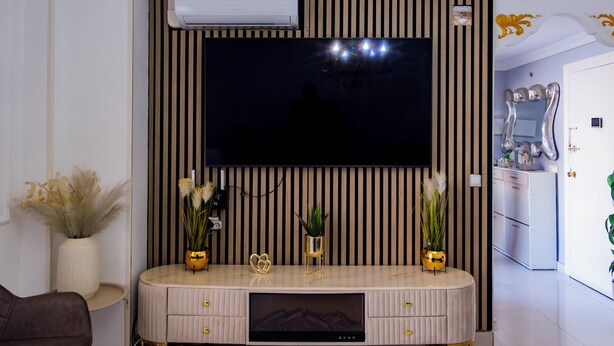 A modern living room with a flat-screen TV mounted on a wall with vertical stripes, a built-in entertainment unit below, and a small plant on the unit.