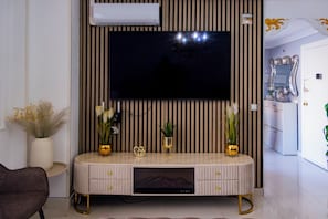 Un salon moderne avec un téléviseur à écran plat fixé au mur, qui présente des rayures verticales, un meuble de rangement intégré en dessous et une petite plante posée sur le meuble.
