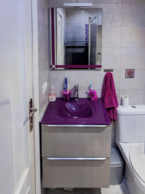 Une salle de bain avec un lavabo violet, un miroir, des toilettes et une poubelle.