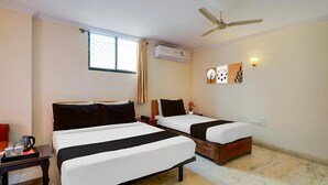 Une chambre d’hôtel avec deux lits, un ventilateur de plafond, un appareil de climatisation, une fenêtre avec des rideaux et un luminaire fixé au mur.