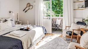 Un dormitorio con cama, mesita de noche, lámpara y vistas al exterior.