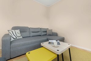 Un salon moderne avec un canapé gris, une petite table blanche sur laquelle se trouvent une tasse et un magazine, et un banc jaune.