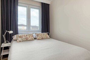 Un lit bien fait, agrémenté d’oreillers à motifs floraux, une table de chevet avec une lampe et une fenêtre avec des rideaux.