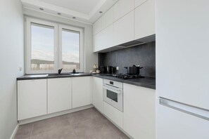 Une cuisine moderne avec des meubles blancs, un plan de travail noir, une fenêtre et une vue sur les bâtiments environnants.