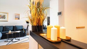 Una sala de estar moderna con un sofá oscuro, una mesita auxiliar pequeña y una planta grande en maceta.