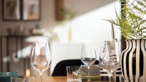 Una mesa de comedor con copas de vino, un florero con helecho y un florero a rayas.