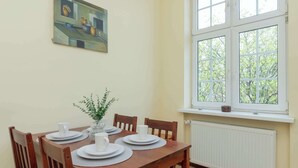 A dining area with a wooden table set for four, a window with a view of trees, and a radiator below.