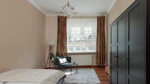 A bedroom with a bed, a desk, a chair, a radiator, and a window with curtains.