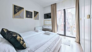 A hotel room with a bed, a TV, a window with curtains, and artwork on the wall.