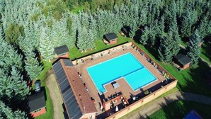 Vista aerea di un complesso piscine circondato da alberi, con una zona coperta e edifici adiacenti.