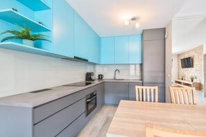 A modern kitchen with grey cabinets, a wooden dining table, and a brick accent wall.