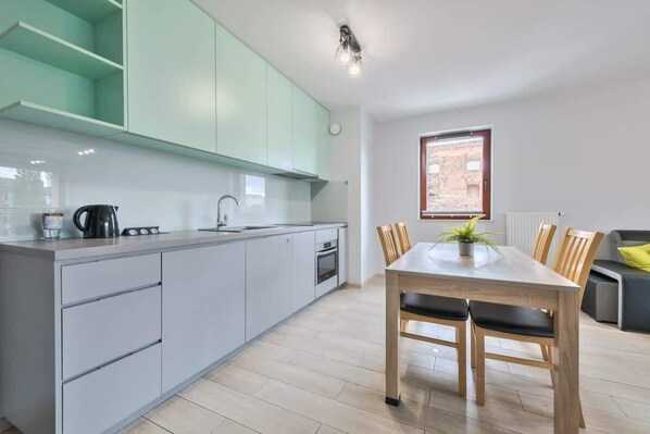 A modern kitchen with light grey cabinets, a wooden dining table with four chairs, and a window with a view of a brick building.
