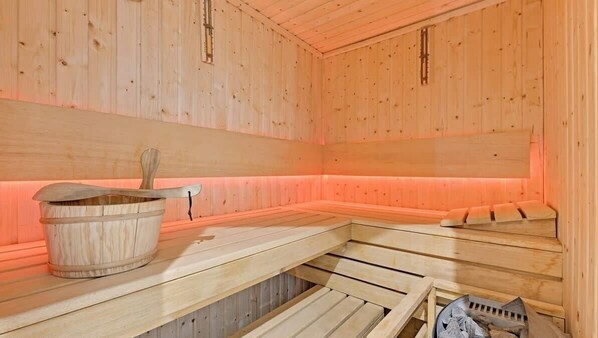 A wooden sauna with benches, a wooden bucket, and a grate for burning wood.