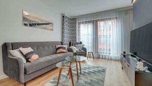 A modern living room with a grey sofa, a glass coffee table, and a flat-screen TV.