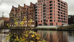 A riverside view of a historic building with a modern high-rise building adjacent to it.