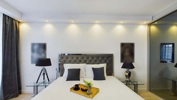 Un dormitorio de hotel moderno con una cama grande, lámparas de noche, una mesita de vidrio con bandeja y un espejo grande.