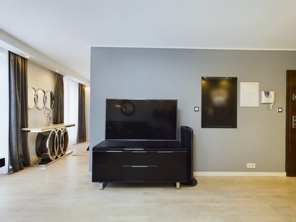 Una sala moderna con un televisor de pantalla plana grande sobre un mueble negro, una pared minimalista con un cuadro enmarcado y un suelo de madera claro.