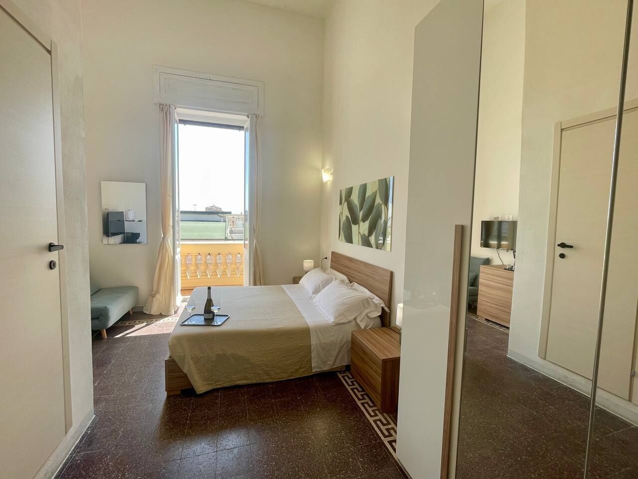 A bedroom with a bed, bedside tables, a nightstand, a window with curtains, a wall-mounted TV, and a door.