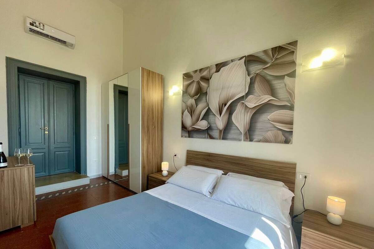 Quarto de hotel com cama, mesas de cabeceira, espelho, guarda-roupa e parede com um mural floral.