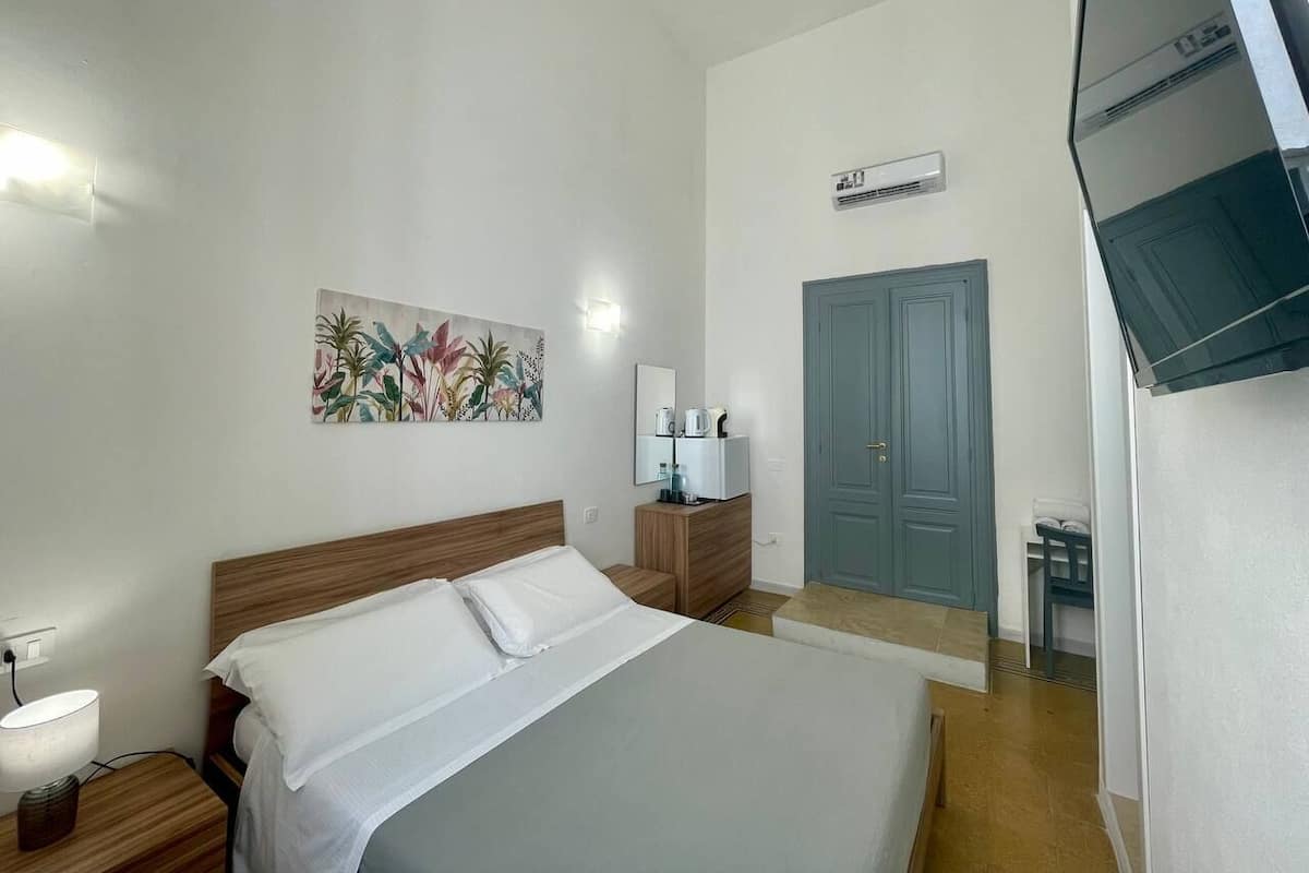 Quarto de hotel com cama, mesa de cabeceira, luminária, obras de arte, cômoda, espelho e uma porta.
