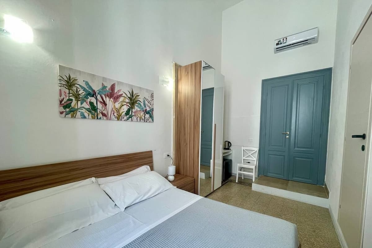 Quarto de hotel com cama, espelho, guarda-roupa, porta e ar-condicionado fixado na parede.