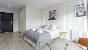 Une chambre à coucher moderne, avec un lit, une table d’appoint ronde, une chaise et des œuvres d’art accrochées aux murs.
