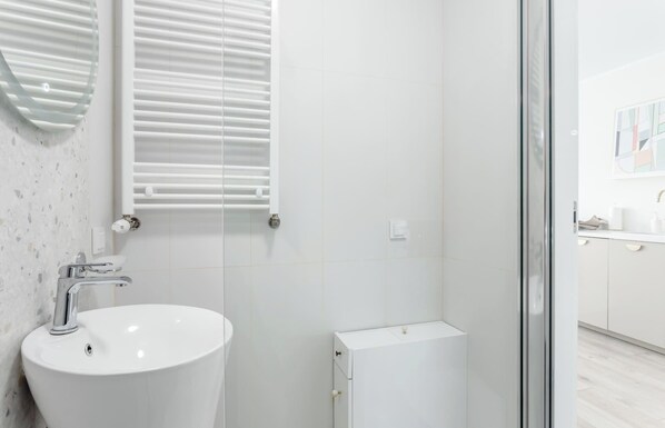 A modern bathroom with a large white sink, a glass shower enclosure, and a small white cabinet.