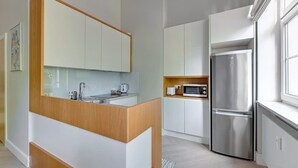 Een moderne keuken met een centraal eiland, witte kasten, roestvrijstalen apparatuur en een raam voor natuurlijk licht.