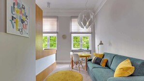 Een moderne woonkamer met een bank, een geel vloerkleed, een eettafel en een groot raam.
