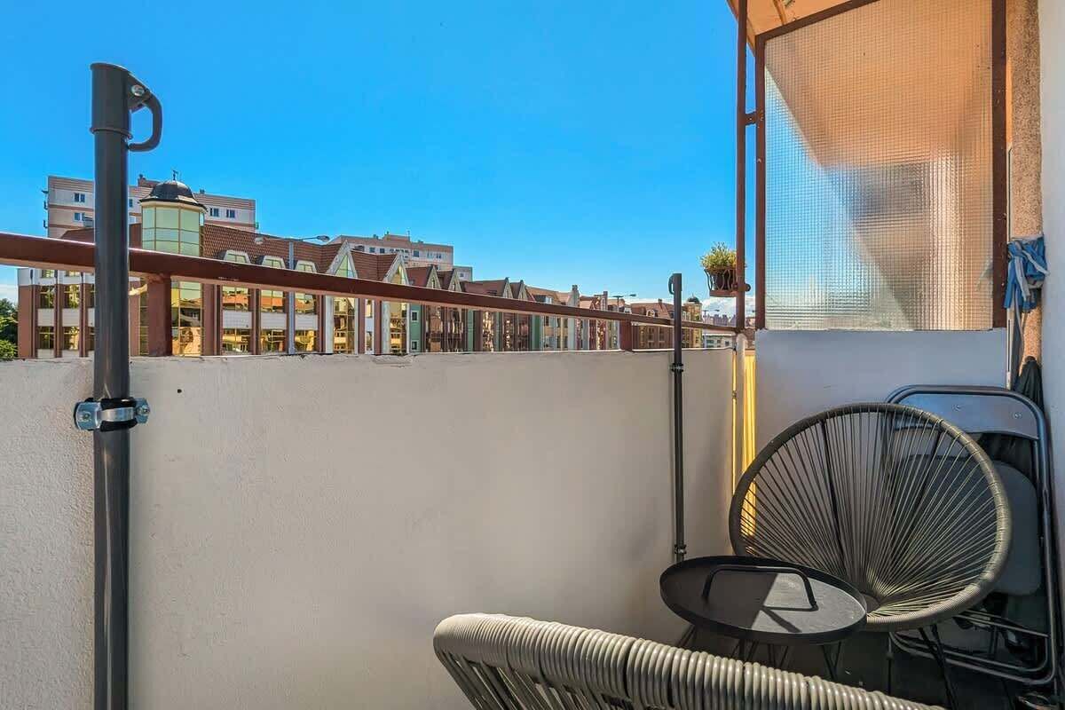 Un balcón con una silla, una planta colgante y vistas a edificios.