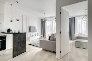 A modern apartment interior with an open-plan living area, a compact kitchen, and a glimpse of a cozy bedroom through a partially open door. - Stylish Apartment with Balcony | Air Conditioning | Parking (Gdańsk)