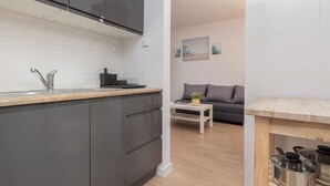 A modern kitchen with dark cabinets, a white countertop, and a stainless steel sink. - Comfortable Studio | Close to the Beach and Reagan Park (Gdańsk)